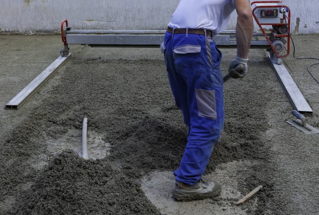 Worker on a laser screed machine leveling fresh poured concrete surface on a construction site